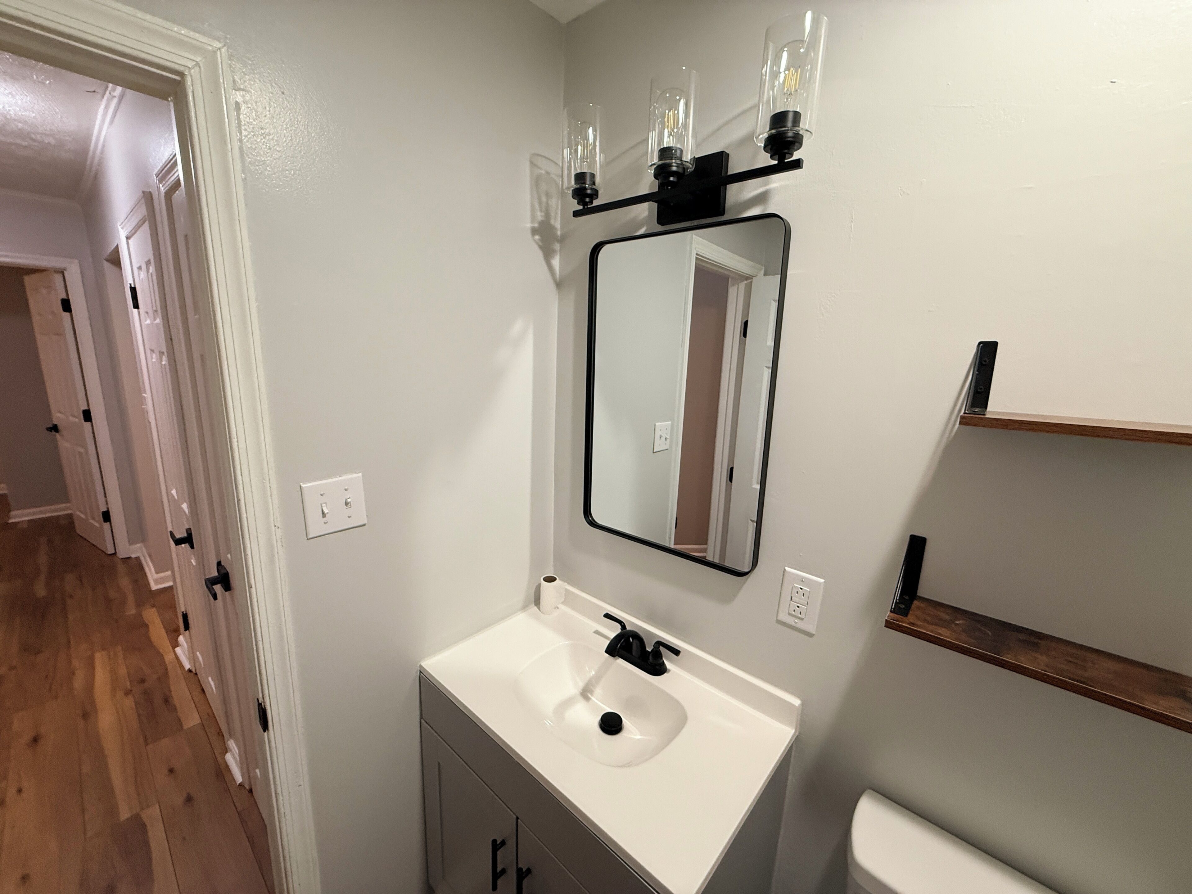 A bathroom with a white sink, a mirror, and a light fixture above the mirror.