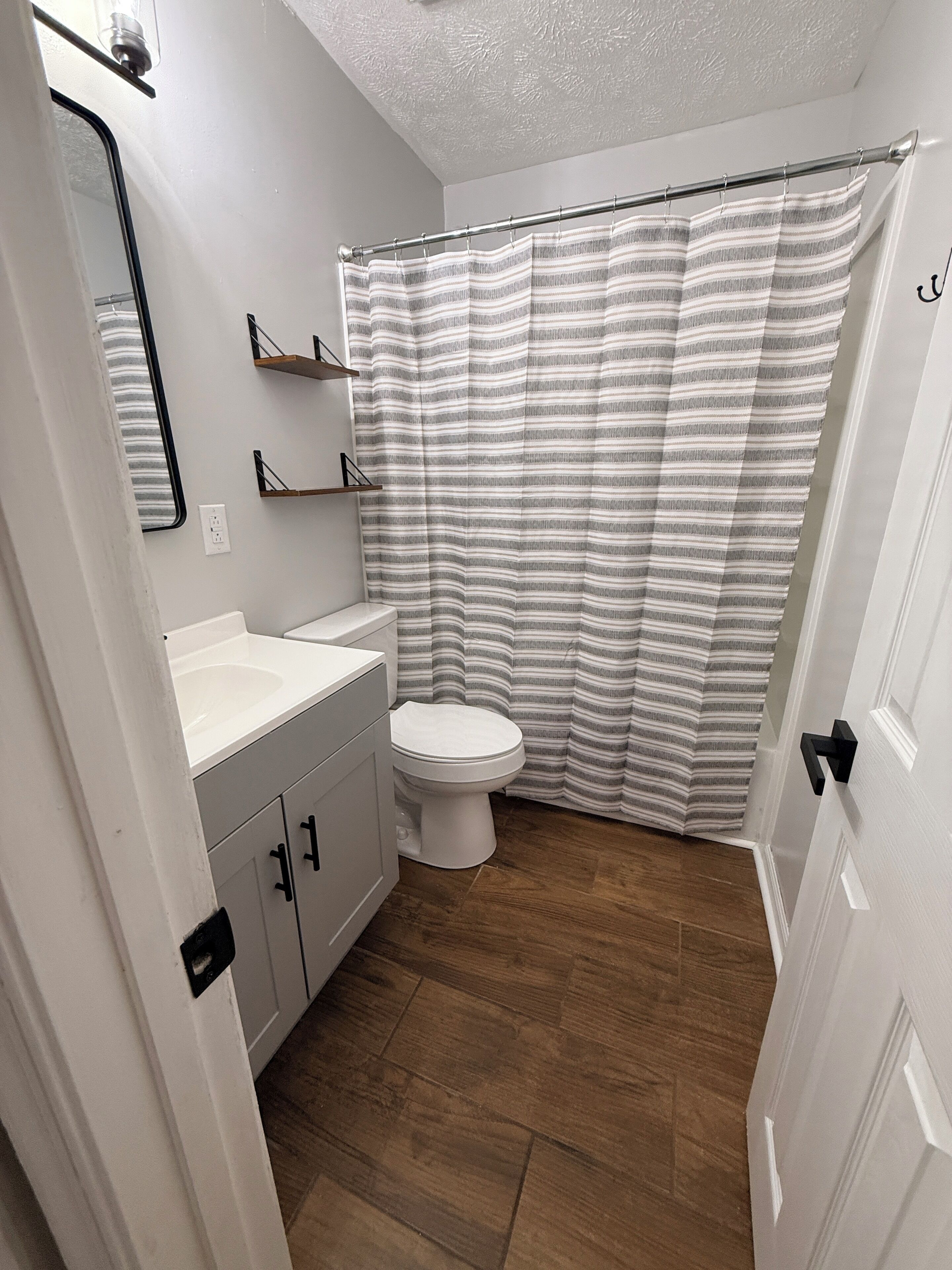 A bathroom with a toilet, a sink, a mirror, and a shower curtain.