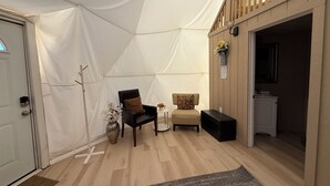 Une pièce aménagée comme une tente, avec un plancher en bois, une chaise noire, une petite table sur laquelle est posé un vase, et un banc.