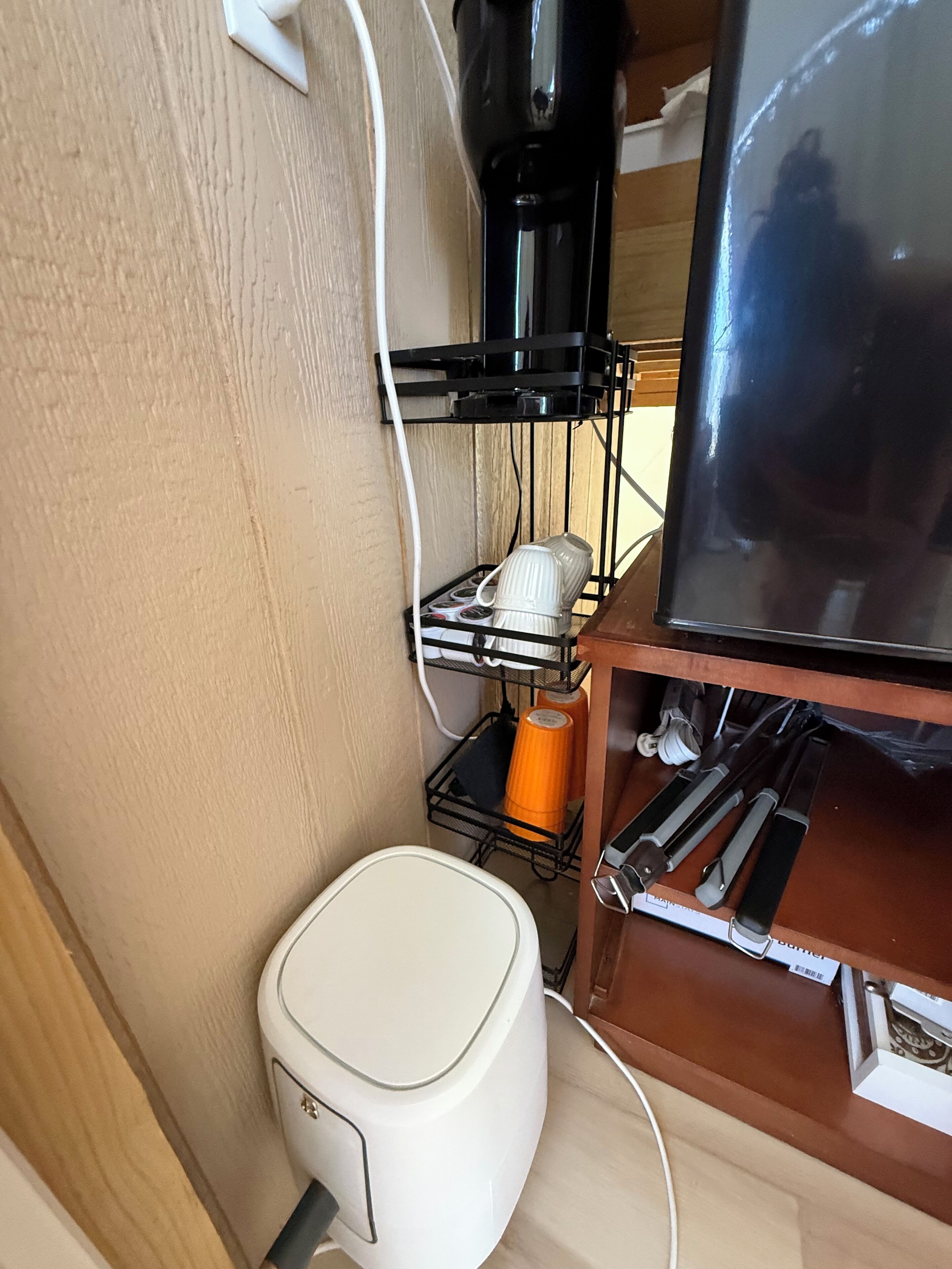 Eine kleine Küchenzeile mit einem weißen Kühlschrank, einer schwarzen Kaffeemaschine und einem Fernseher auf einem Holzboden.