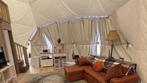 Un hébergement sous tente comprenant un canapé modulable, un petit bureau et une lampe.
