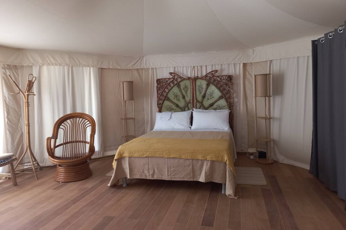 Een slaapkamer met een bed, een stoel, een vloerlamp en een plafondventilator.
