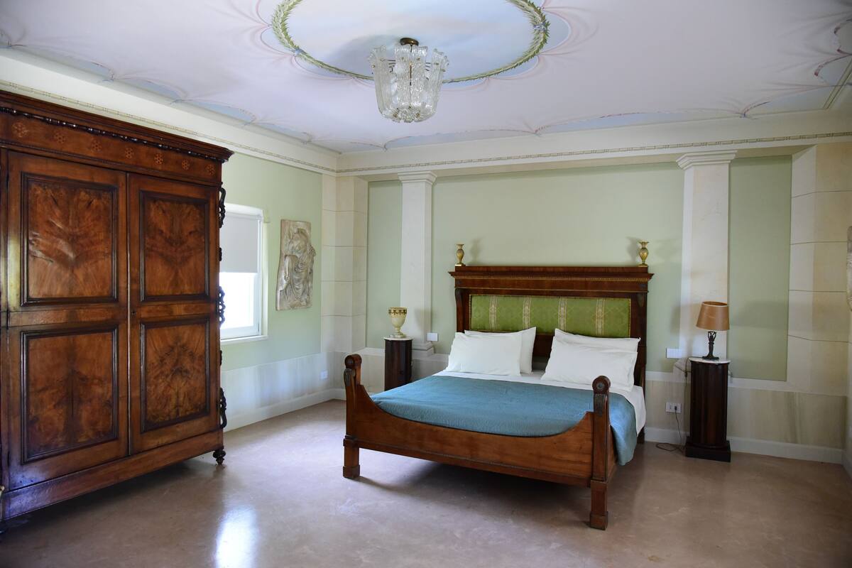 Een slaapkamer met een groot houten bed, een houten kledingkast en een kroonluchter.