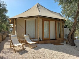 Una estructura pequeña de un solo piso con un toldo color beige, paredes de madera y suelo de grava. Hay dos sillones blancos afuera.
