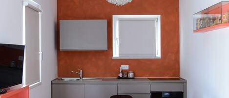 A compact kitchen with a modern design, featuring a white ceiling, an orange accent wall, and a chandelier.