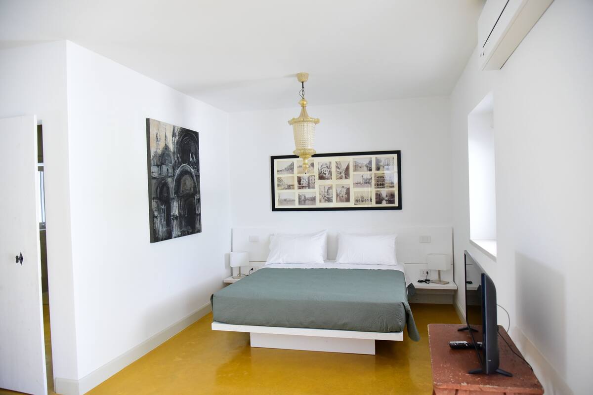 Een slaapkamer met een bed, een kroonluchter, een lijst met foto's en een televisie op een houten tafel.