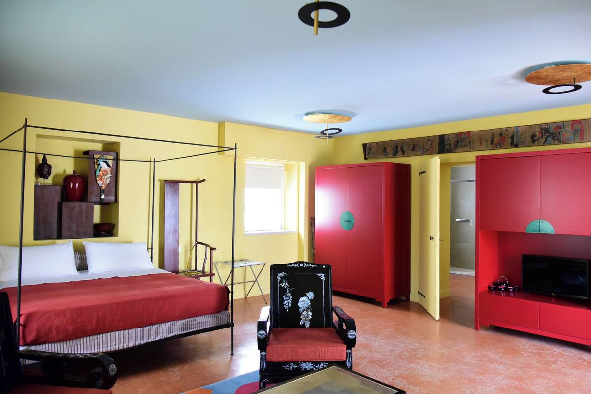 Een kamer met een hemelbed, een rode bank, een televisie en een rode garderobe.