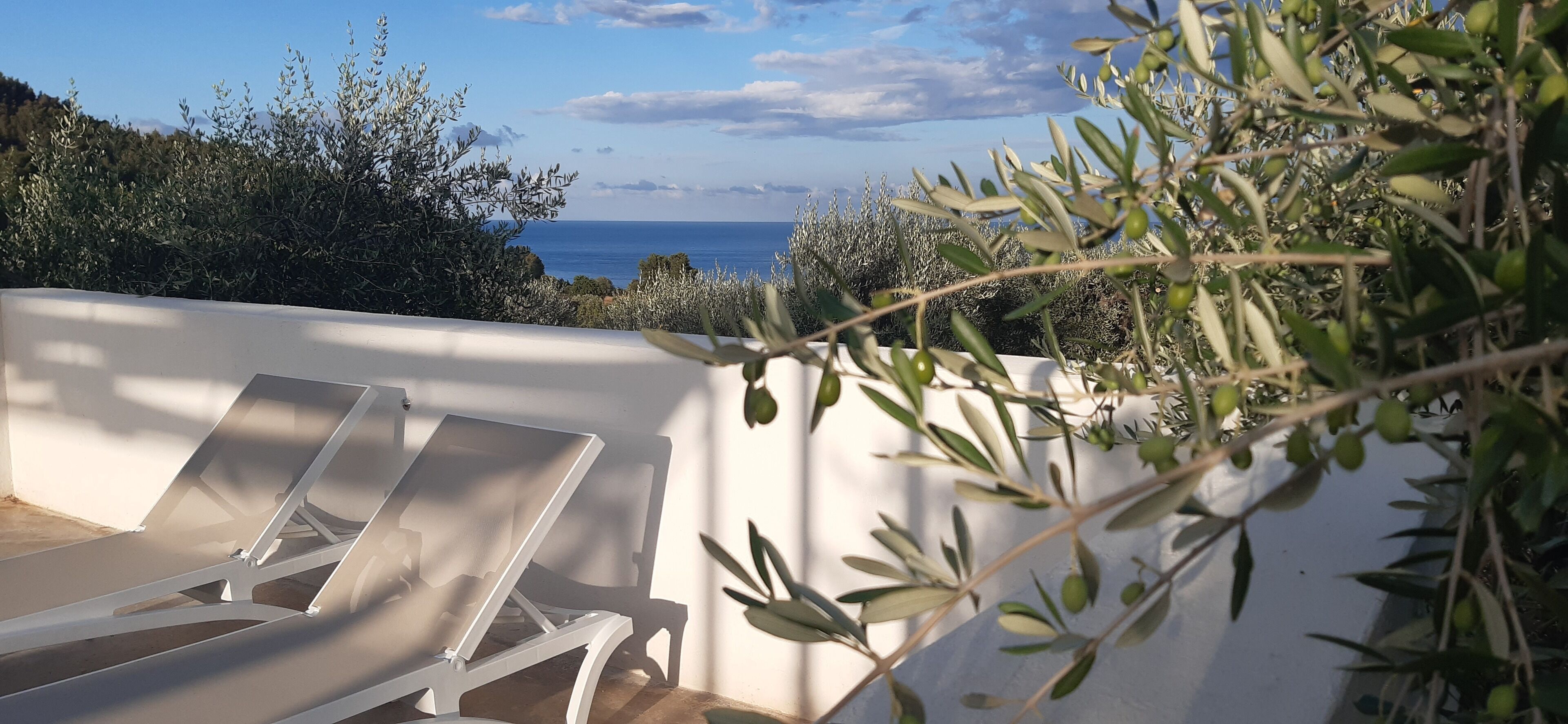 Una terraza con sillones blancos y vista al mar.