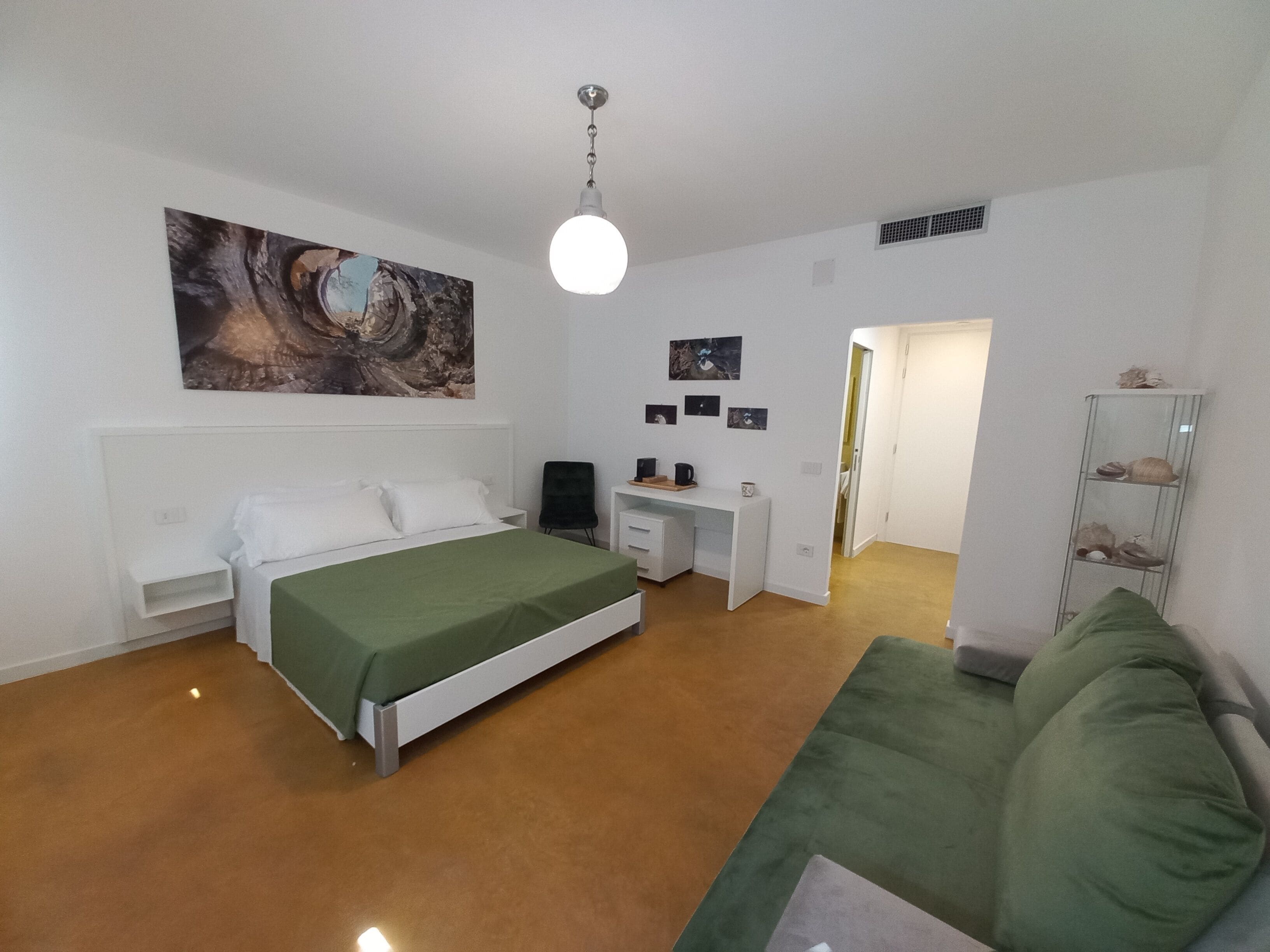 A bedroom with a bed, a desk, a chair, a green sofa, and a wall with artwork.