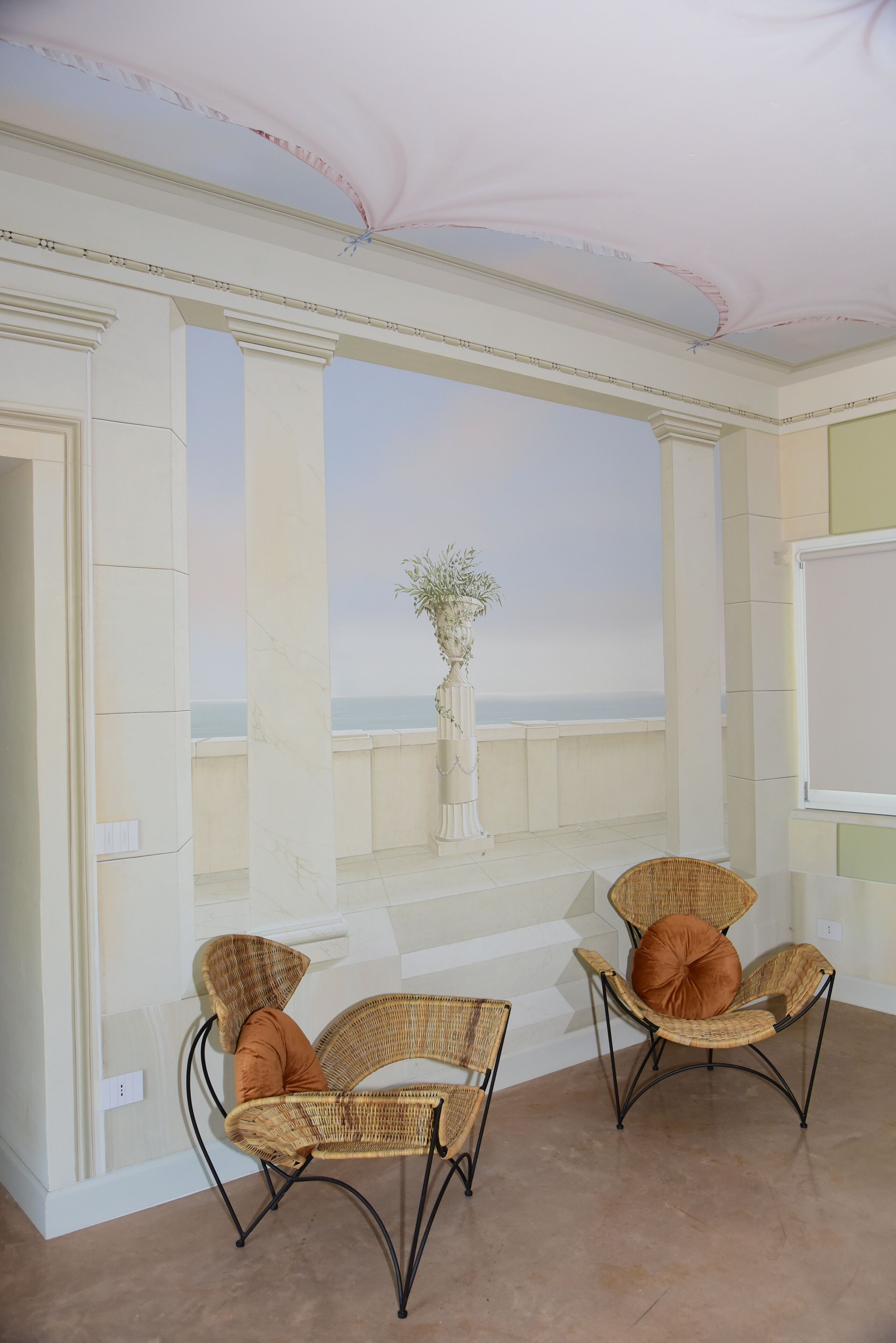 A room with two wicker chairs, a potted plant, and a view of the sea.