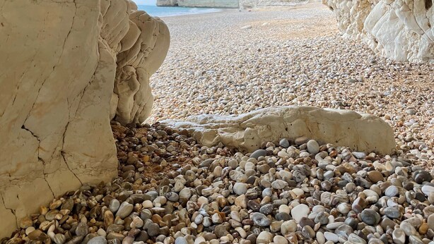 A pebbled beach with a rocky cave entrance.