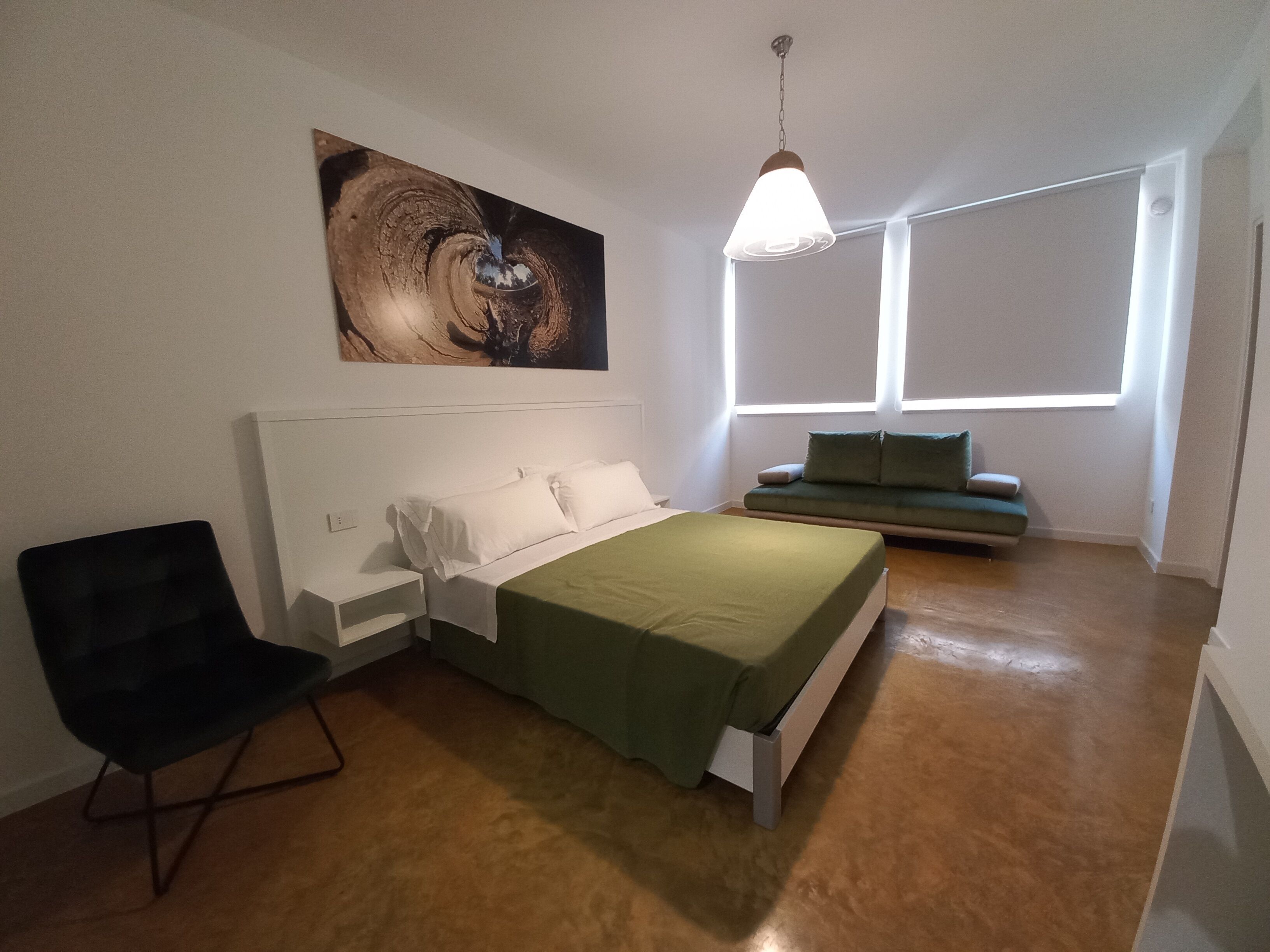 A bedroom with a bed, a chair, a sofa, a painting, and a window.