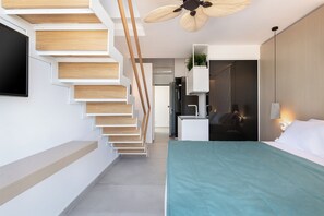 Une chambre moderne avec un escalier, un lit, une télévision et un coin cuisine.