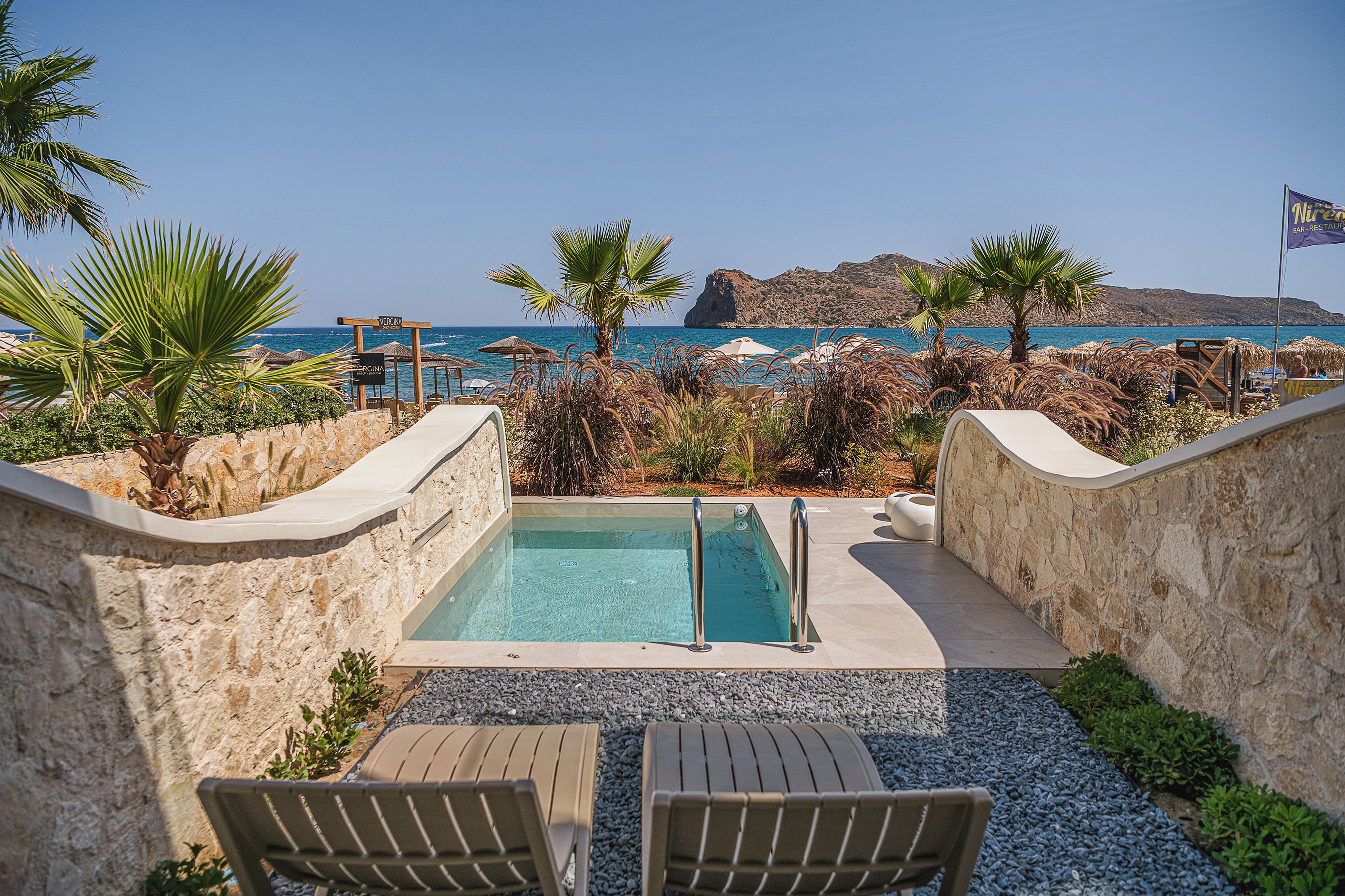 Zona de piscina con vista al mar, rodeada de palmeras y sillones de descanso.