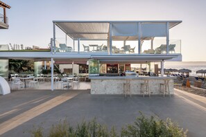 Un espace bar extérieur moderne, doté de sièges, d’un comptoir en pierre et offrant une vue sur la mer.