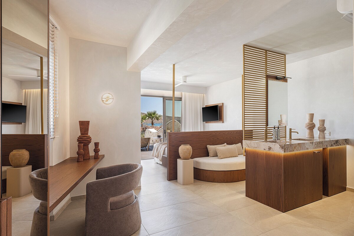 A modern hotel room with a large bed, a wooden vanity, and a seating area with a view of the ocean.