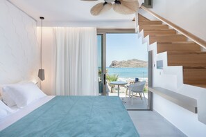 A modern hotel room with a bed, a view of the sea, a staircase, and a balcony with outdoor seating. - Vergina Beach Resort (Chania)