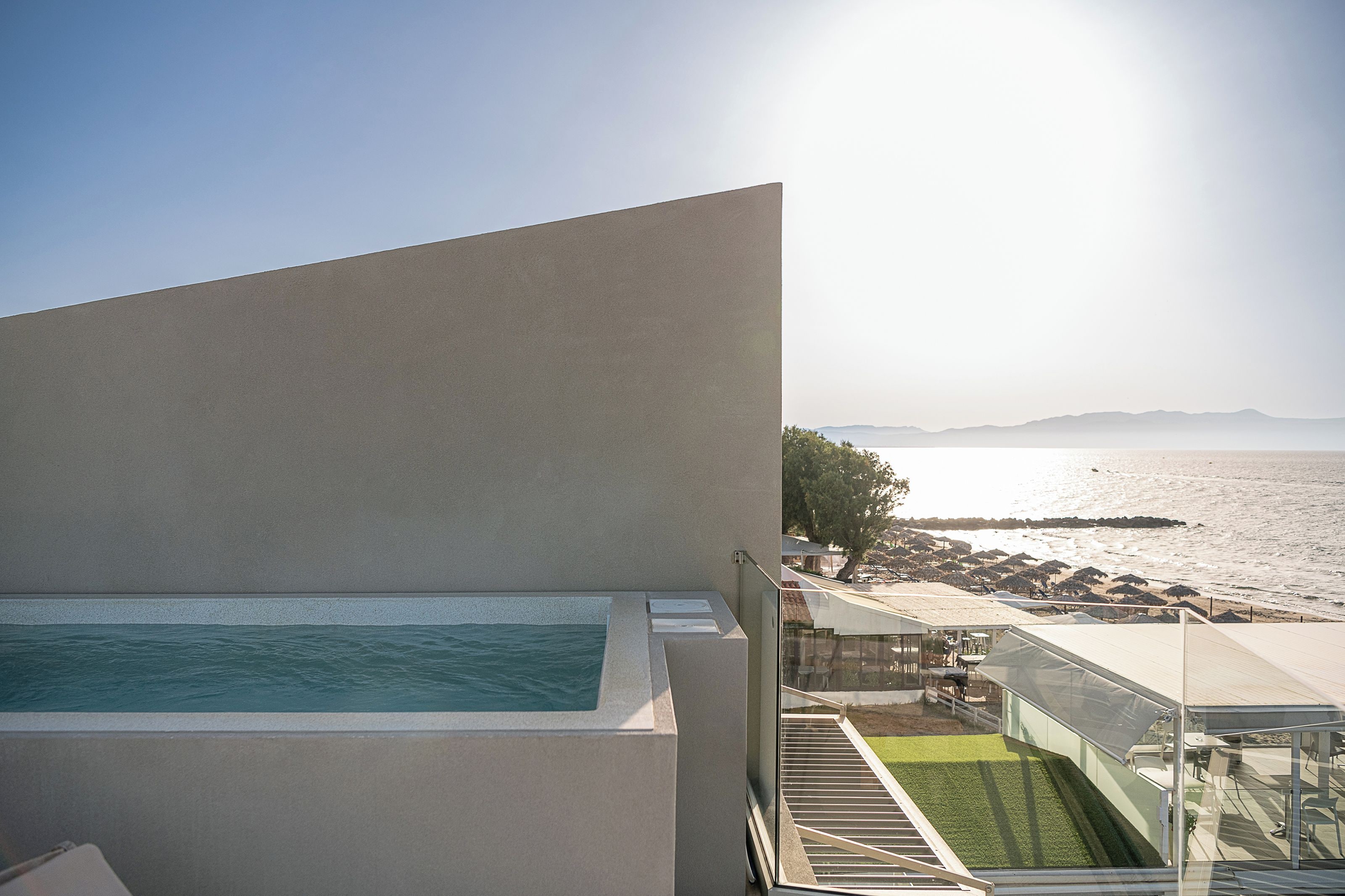 A modern building with a pool, a terrace with a view of the sea, and a covered outdoor seating area.