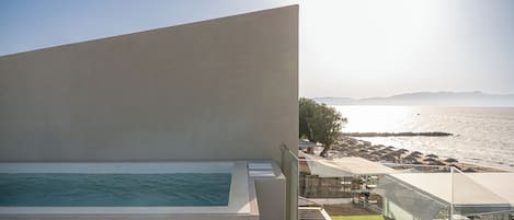 A modern building with a pool, a terrace with a view of the sea, and a covered outdoor seating area.