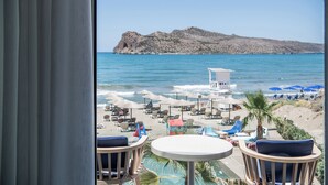A beach view from a balcony with a table and chairs, umbrellas, and a lifeguard tower. - Vergina Beach Resort (Chania)
