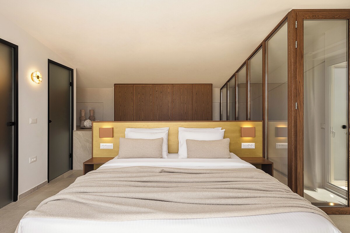A hotel room with a large bed, wooden headboard, bedside lamps, and a large mirror.