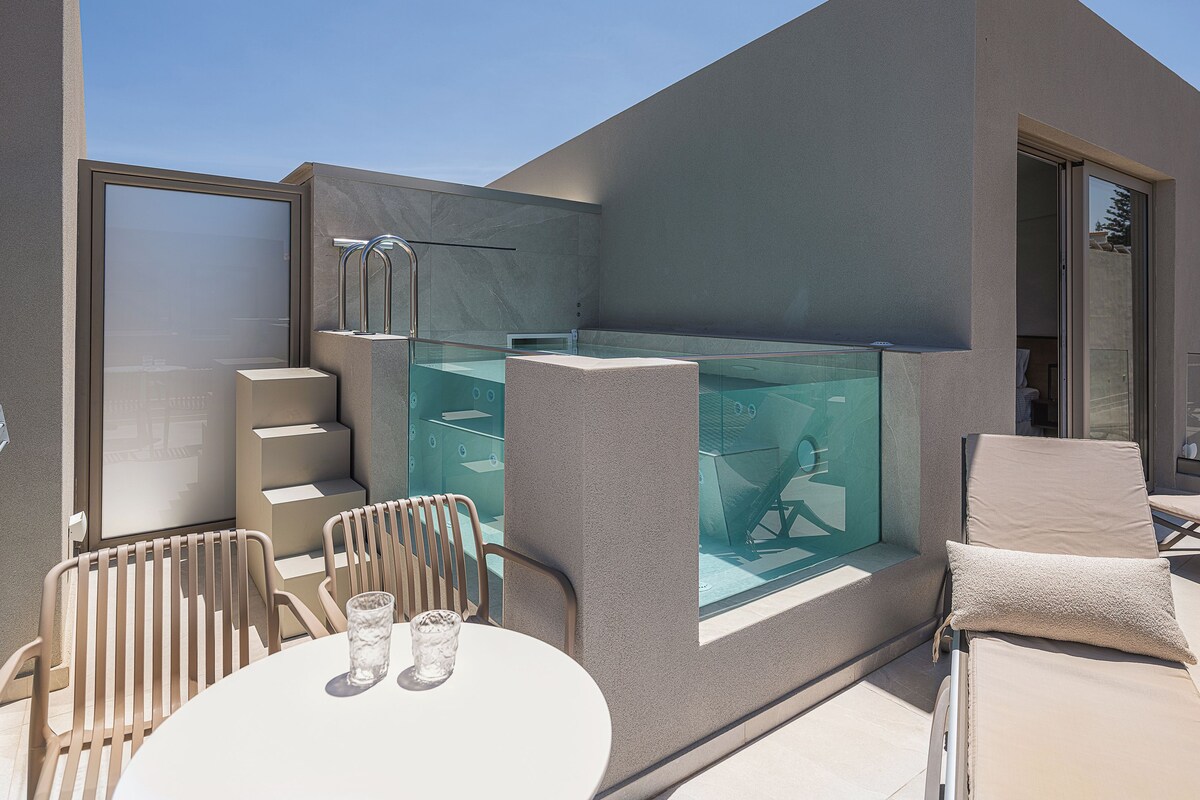 A modern outdoor seating area with a glass-enclosed pool, a table with chairs, and a sun lounger.