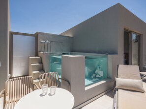 A modern outdoor seating area with a glass-enclosed pool, a table with chairs, and a sun lounger. - Vergina Beach Resort (Chania)