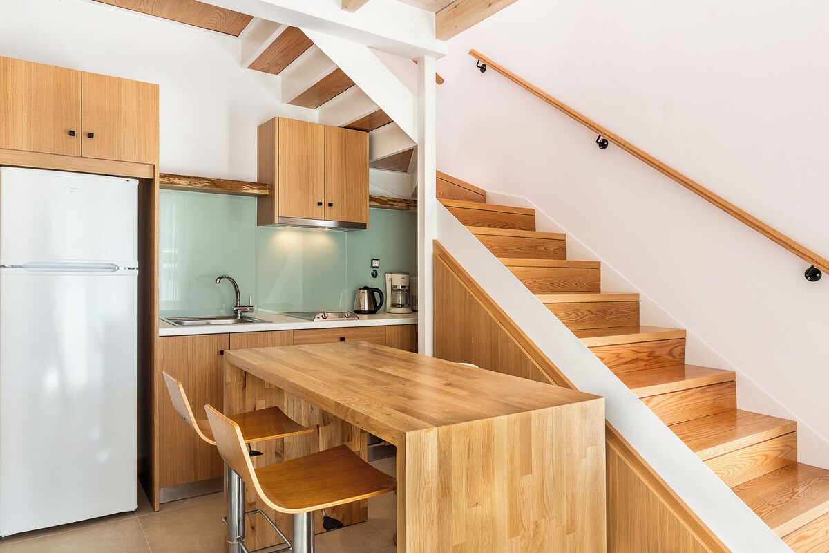 Een moderne keuken met houten kastjes, een ingebouwde kookplaat en een houten eettafel met barstoelen.