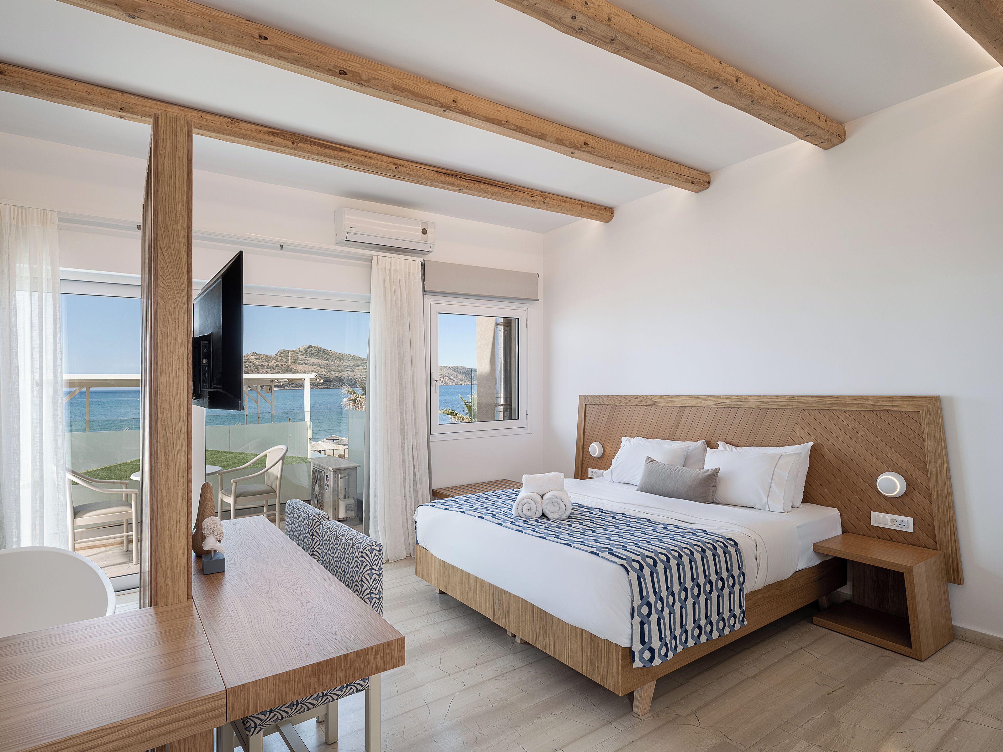 Een slaapkamer met een bed, nachtkastje en uitzicht op zee.