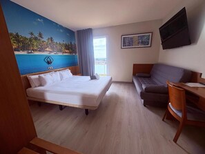 A hotel room with a bed, a sofa, a desk, a TV, and a painting of a beach scene. - Futurotel Cambrils Paradise Resort (Vinyols i els Arcs)