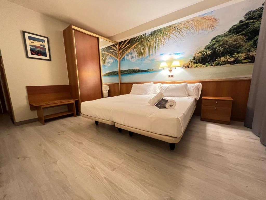 Una habitación de hotel con una cama, un banco, una mesita de noche y un cuadro de una playa.