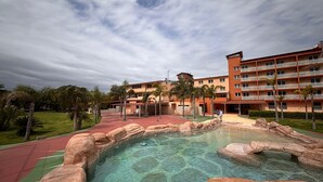 Hotel met zwembad, omringd door rotsen, een rode atletiekbaan en palmbomen.