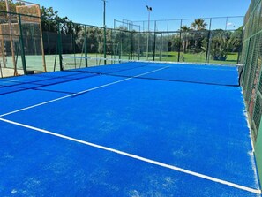 Un court de tennis avec une surface bleue et des lignes de démarcation blanches, entouré d’une clôture verte.