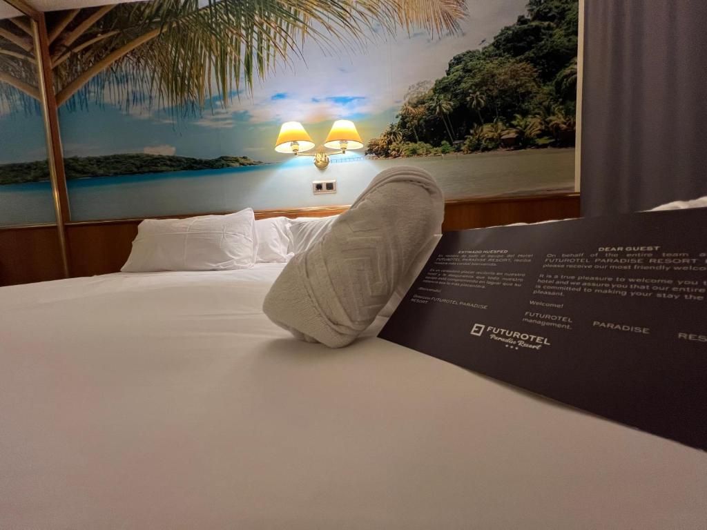Habitación de hotel con cama, mesita de noche con lámparas y un mural con paisaje de playa.