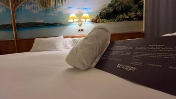 Habitación de hotel con cama, mesita de noche con lámparas y un mural con paisaje de playa.