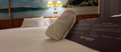 Habitación de hotel con cama, mesita de noche con lámparas y un mural con paisaje de playa.