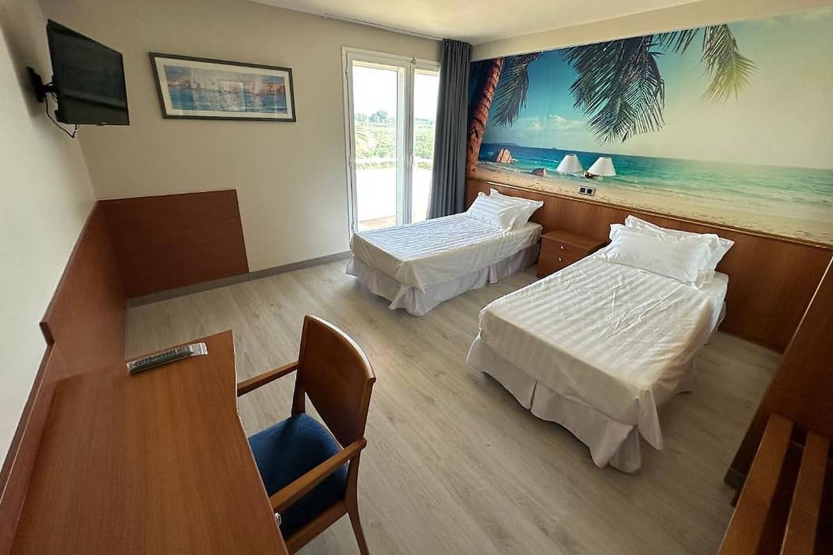 A hotel room with two beds, a desk, a chair, a TV, and a beach mural on the wall.