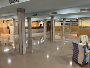 A spacious lobby with a reception desk, a seating area with a chair, and a view of a body of water through the glass walls. - Futurotel Cambrils Paradise Resort (Vinyols i els Arcs)