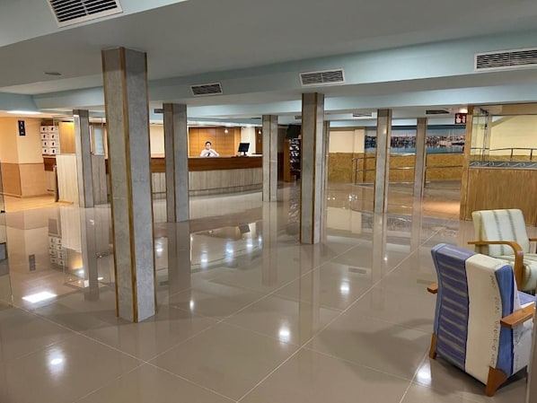 A spacious lobby with a reception desk, a seating area with a chair, and a view of a body of water through the glass walls. - Futurotel Cambrils Paradise Resort (Vinyols i els Arcs)