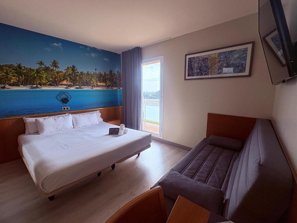 Une chambre d’hôtel avec un grand lit, un canapé, un tableau et une vue sur la mer.