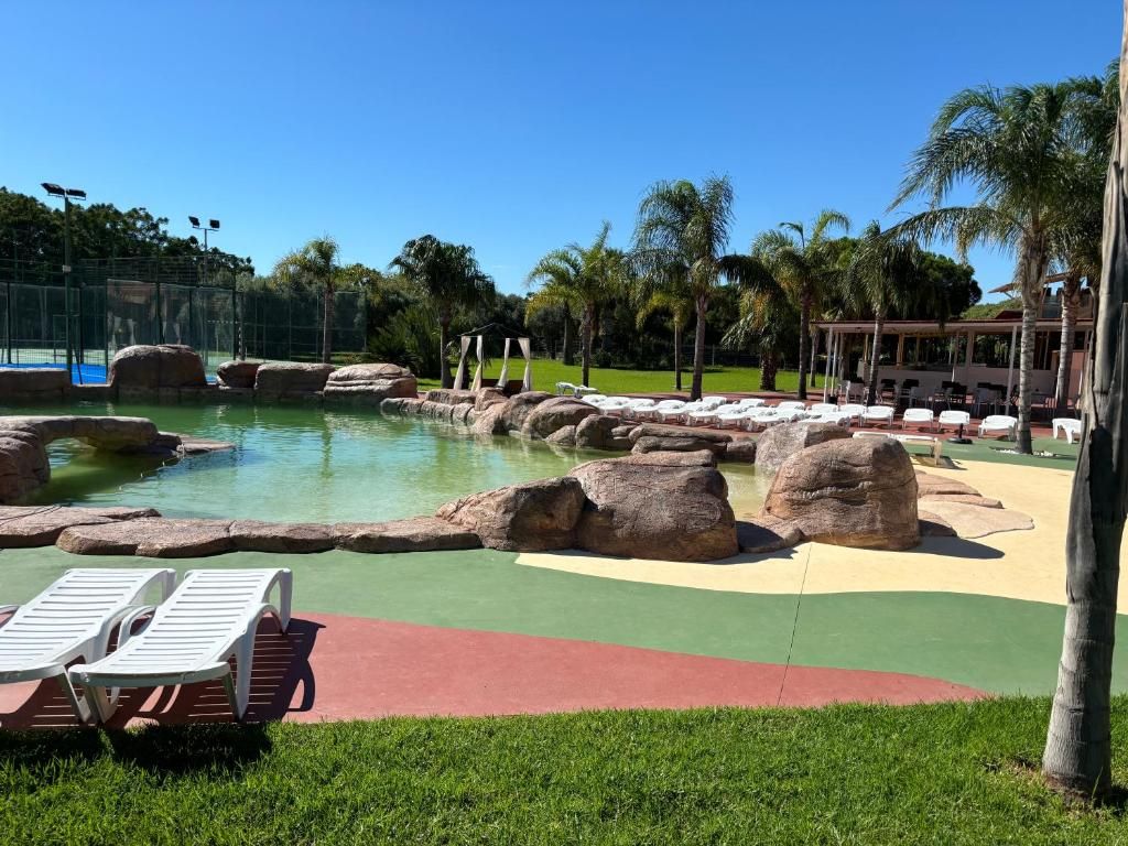 Un área de piscina con rocas grandes, sillas de descanso y palmeras.