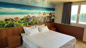 A bedroom with a bed, nightstands, a wooden dresser, and a beach mural on the wall.