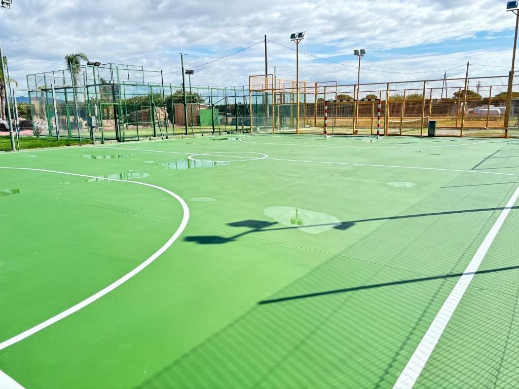 Una cancha de tenis al aire libre con superficie verde, rodeada por una valla y equipada con iluminación artificial.