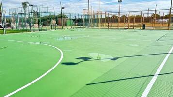 Una cancha de tenis al aire libre con superficie verde, rodeada por una valla y equipada con iluminación artificial.