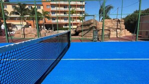 Un court de tennis avec un filet, entouré d’une clôture verte et de palmiers.