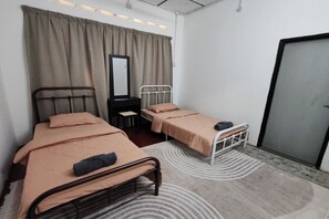 A small, neatly arranged bedroom with two single beds, a desk, a chair, a mirror, and a door.