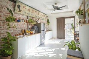 A modern kitchen with a brick wall, a ceiling fan, and a sign above the counter. - Sleepy Nomad Hostel (Malacca City)