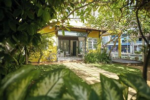 A courtyard with a yellow building, a bicycle, and potted plants. - Sleepy Nomad Hostel (Malacca City)