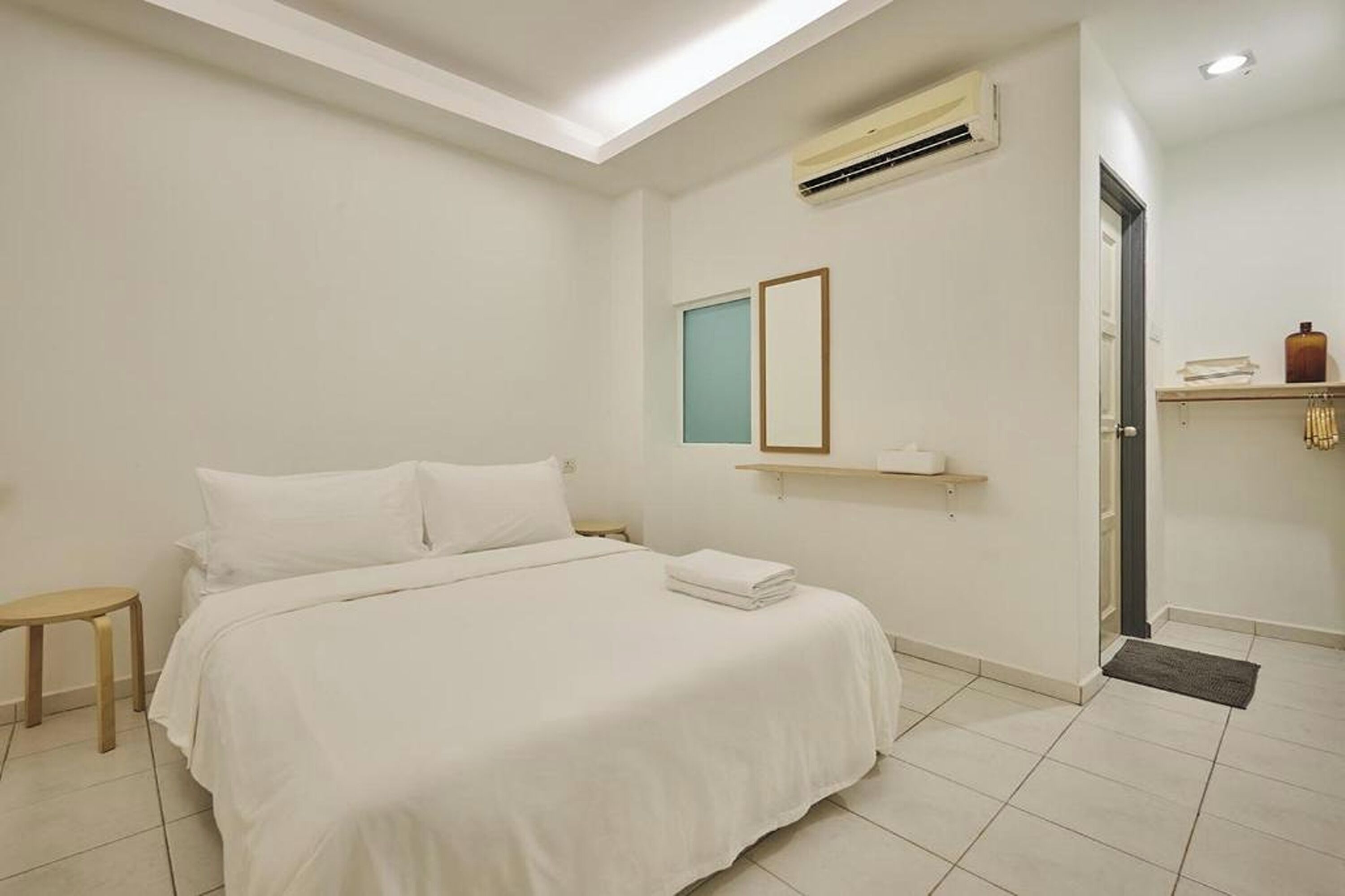 Une chambre d’hôtel comprenant un lit, une petite table de chevet, un climatiseur fixé au mur, une fenêtre et une porte.