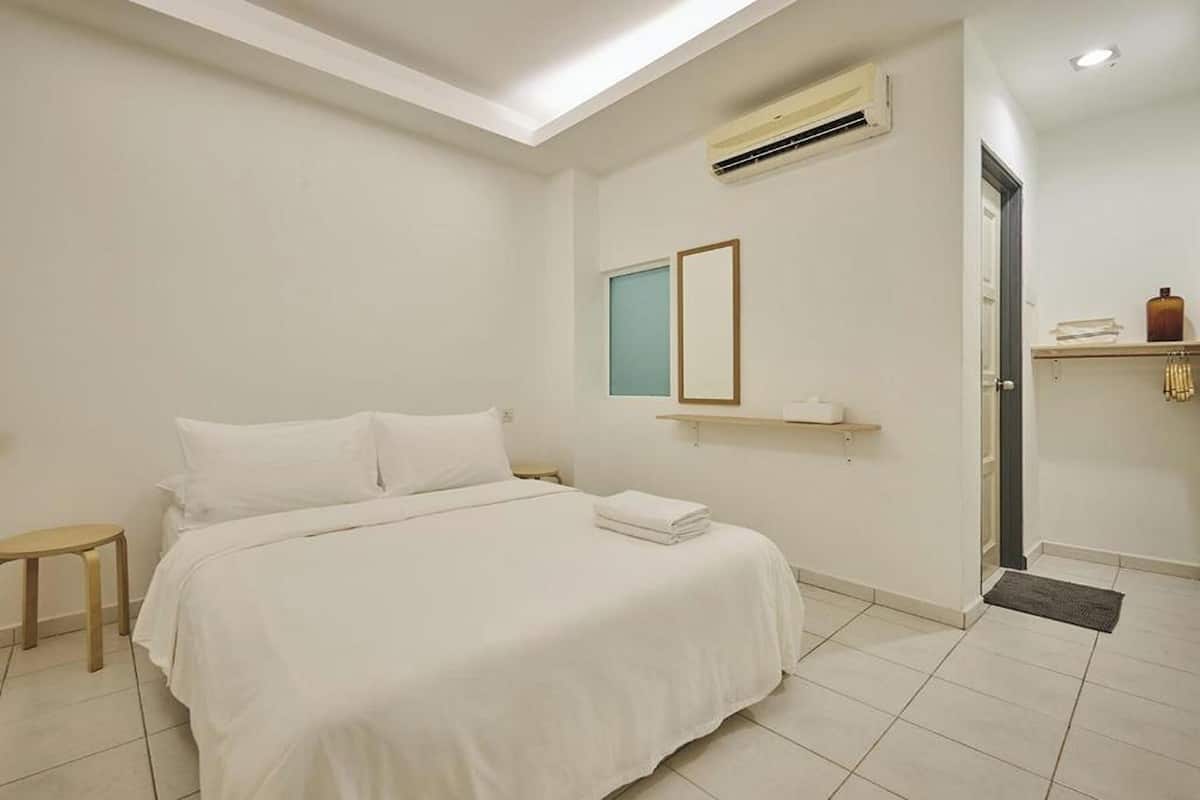 A hotel room with a bed, a small bedside table, a wall-mounted air conditioner, a window, and a door.